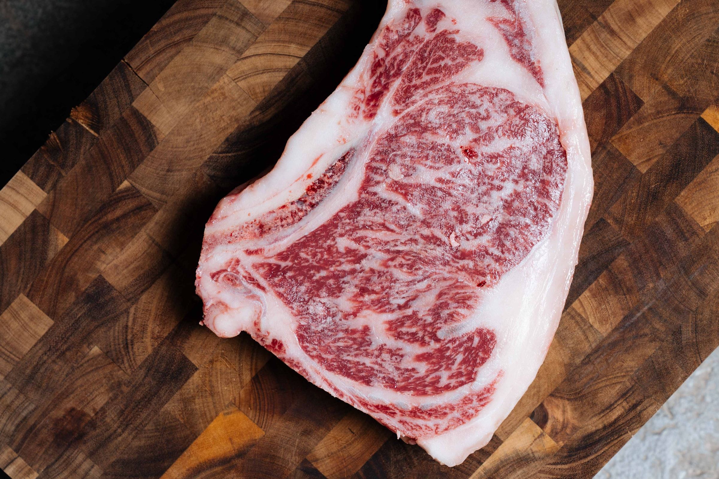Een rauwe entrecôte van Tajiri met fijne, gelijkmatige marmering op een snijplank van kopshout