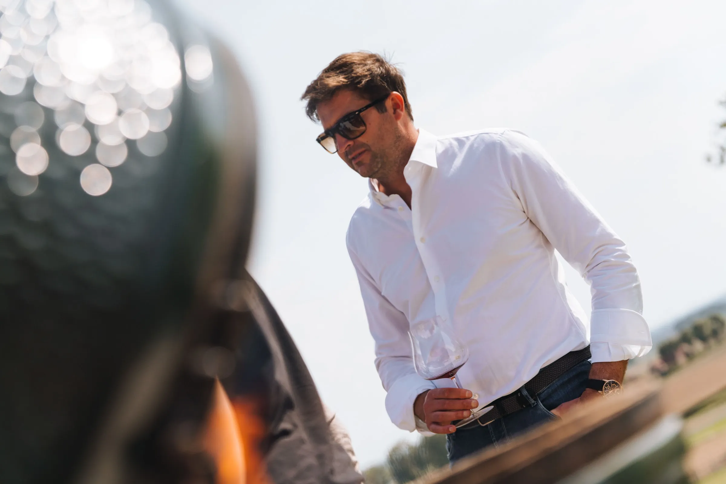 Olivier Monteyne in een wit hemd met een glas wijn bij het vuur van de kamado