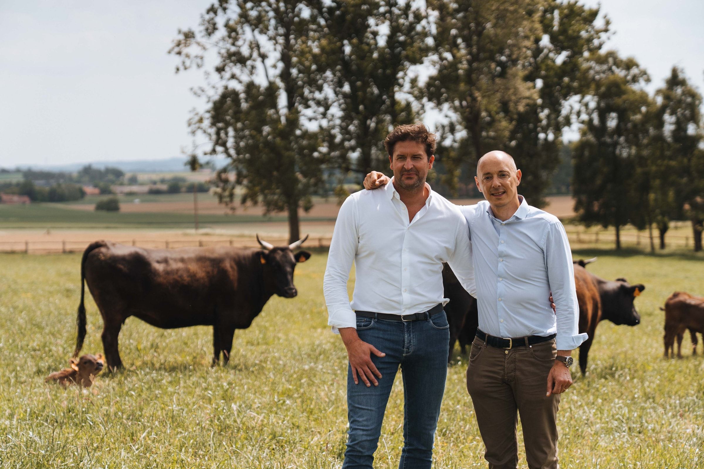 Olivier Monteyne (links) en Arnaud Vandenbogaerde staan lachend in de weide, met hun Wagyu-runderen achter hen