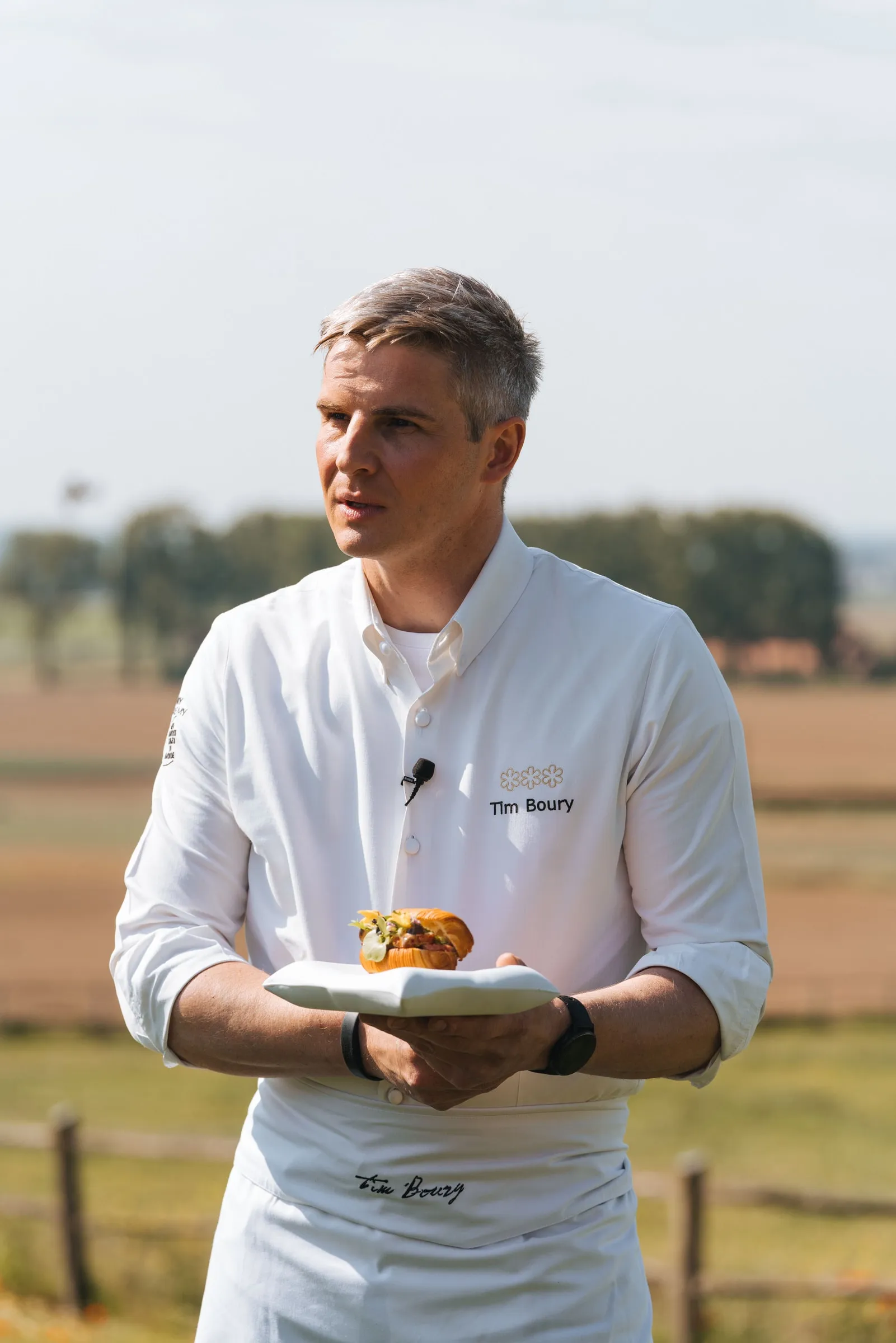 Chef Tim Boury met zijn gerecht in de hand, aan de rand van de weide